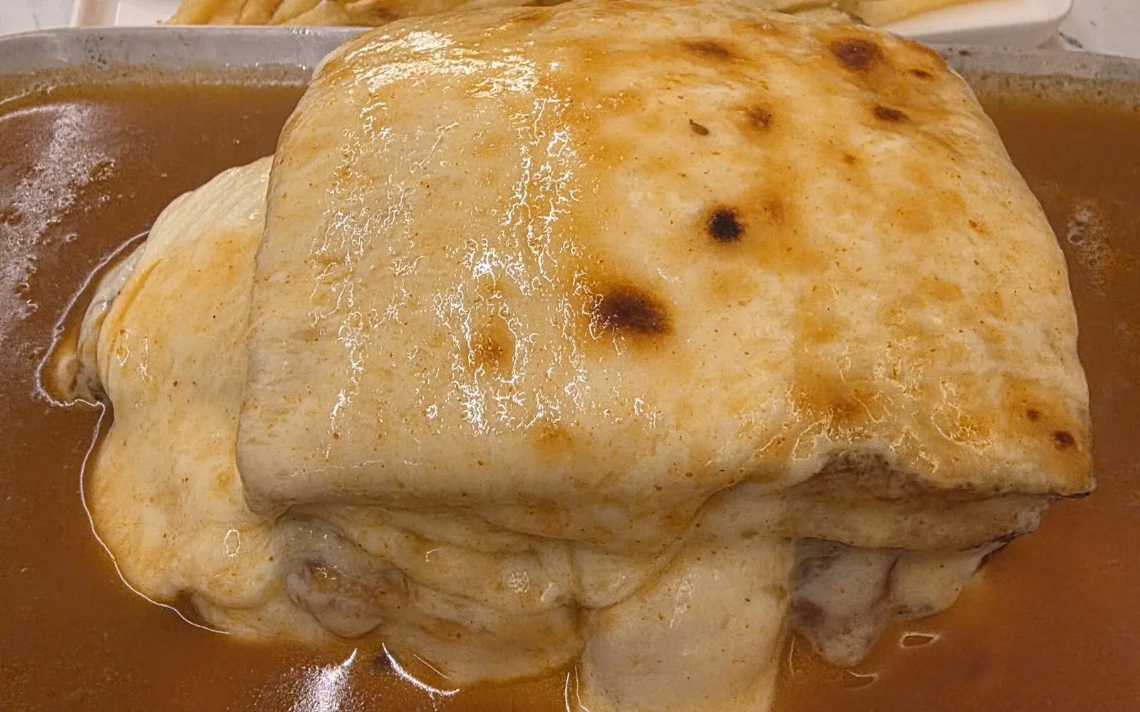 Francesinha da Musa em pão focaccia, com o queijo a derreter no molho e um prato de batata frita.