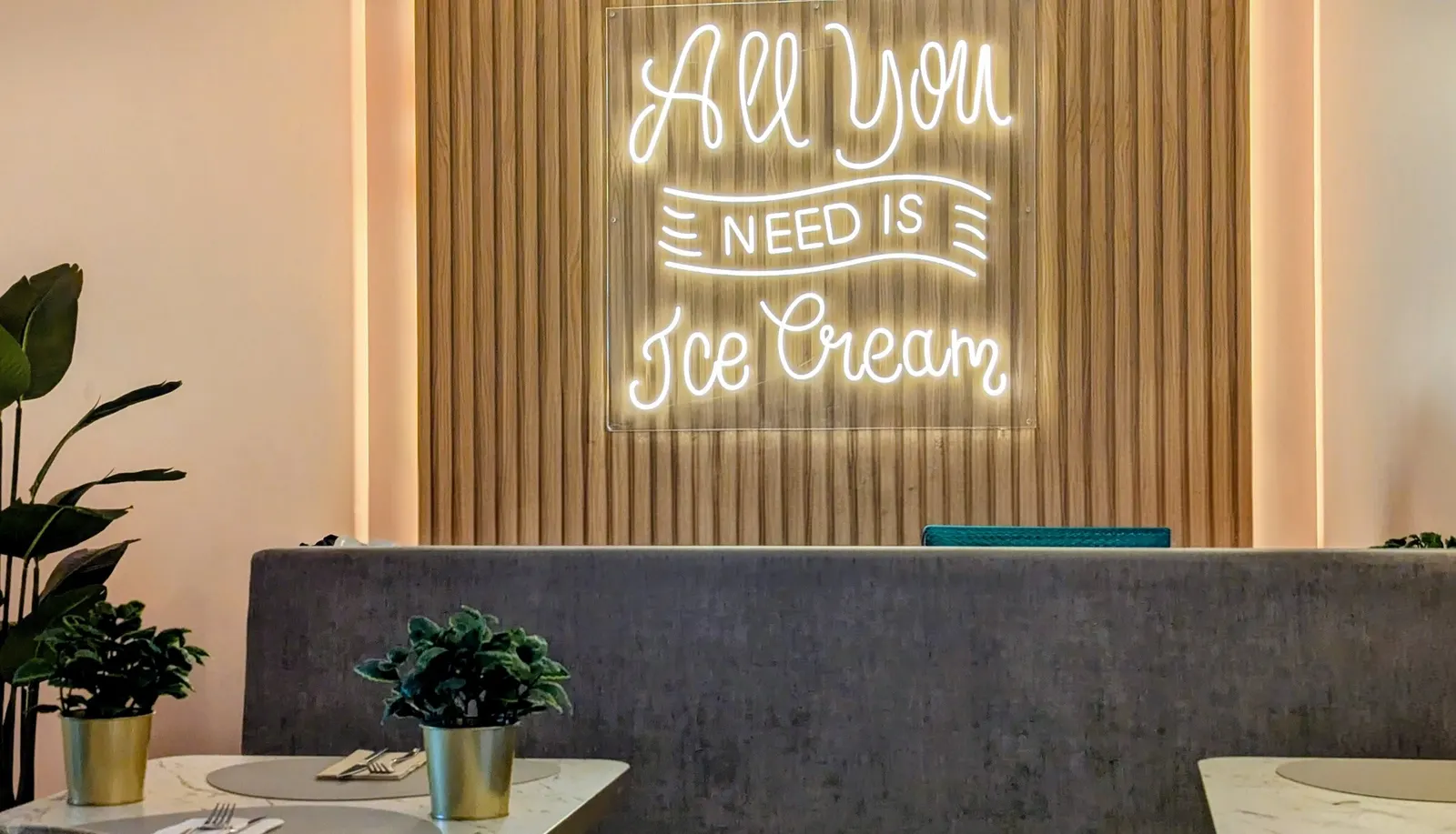 O néon branco “All you need is Ice Cream” na parede de ripas de madeira da Musa, por cima de um banco cinzento.
