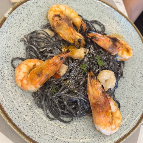 Massa negra com camarões grelhados, num prato azul-claro.