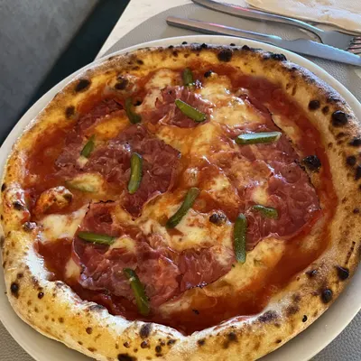 Pizza Al Pastrami vista de cima, com pastrami e pickles de pepino, na mesa da Musa.